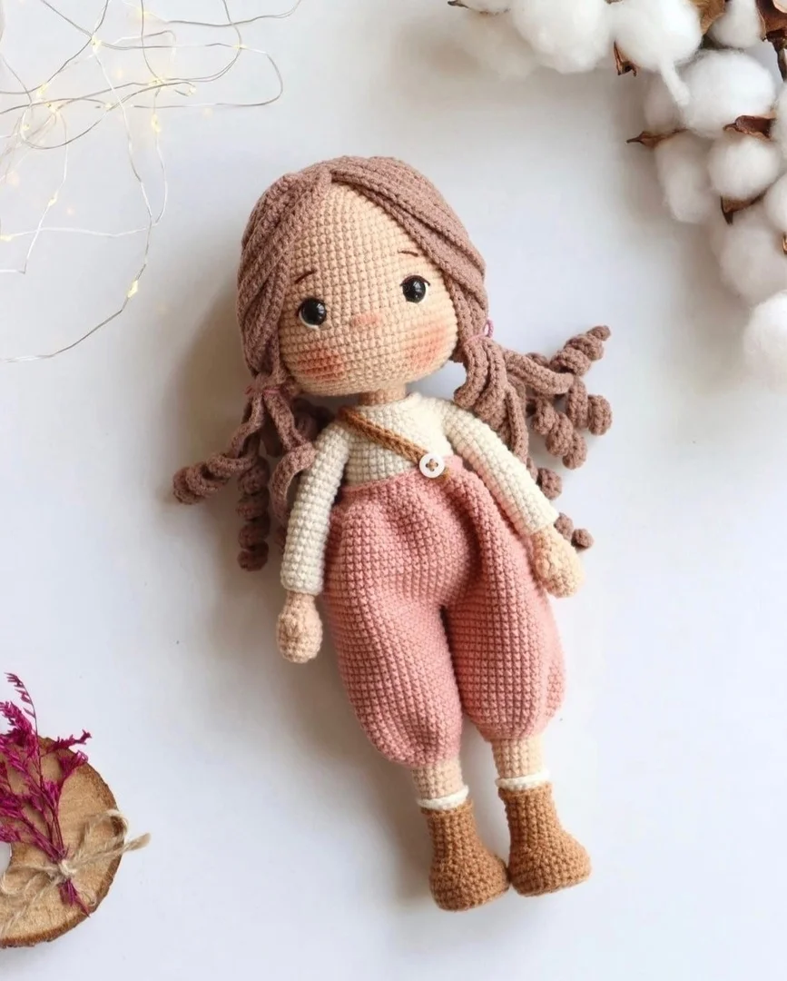 Búp bê cô gái len móc màu hồng nằm trên nền trắng
